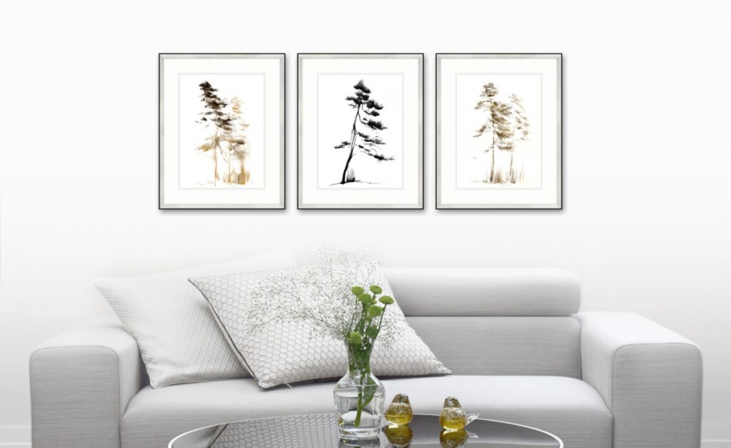 Zdjęcie przedstawiające trzy obrazy z motywem drzew wiszące nad jasną prostą kanapą