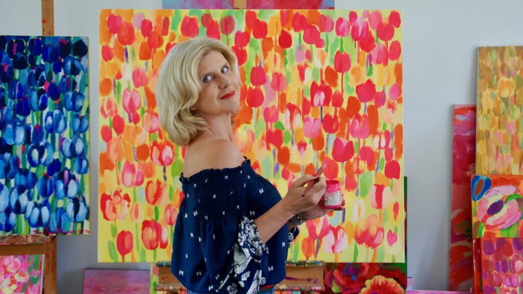 Artystka Beata Murawska stojąca przed kolorowymi obrazami przedstawiającymi tulipany