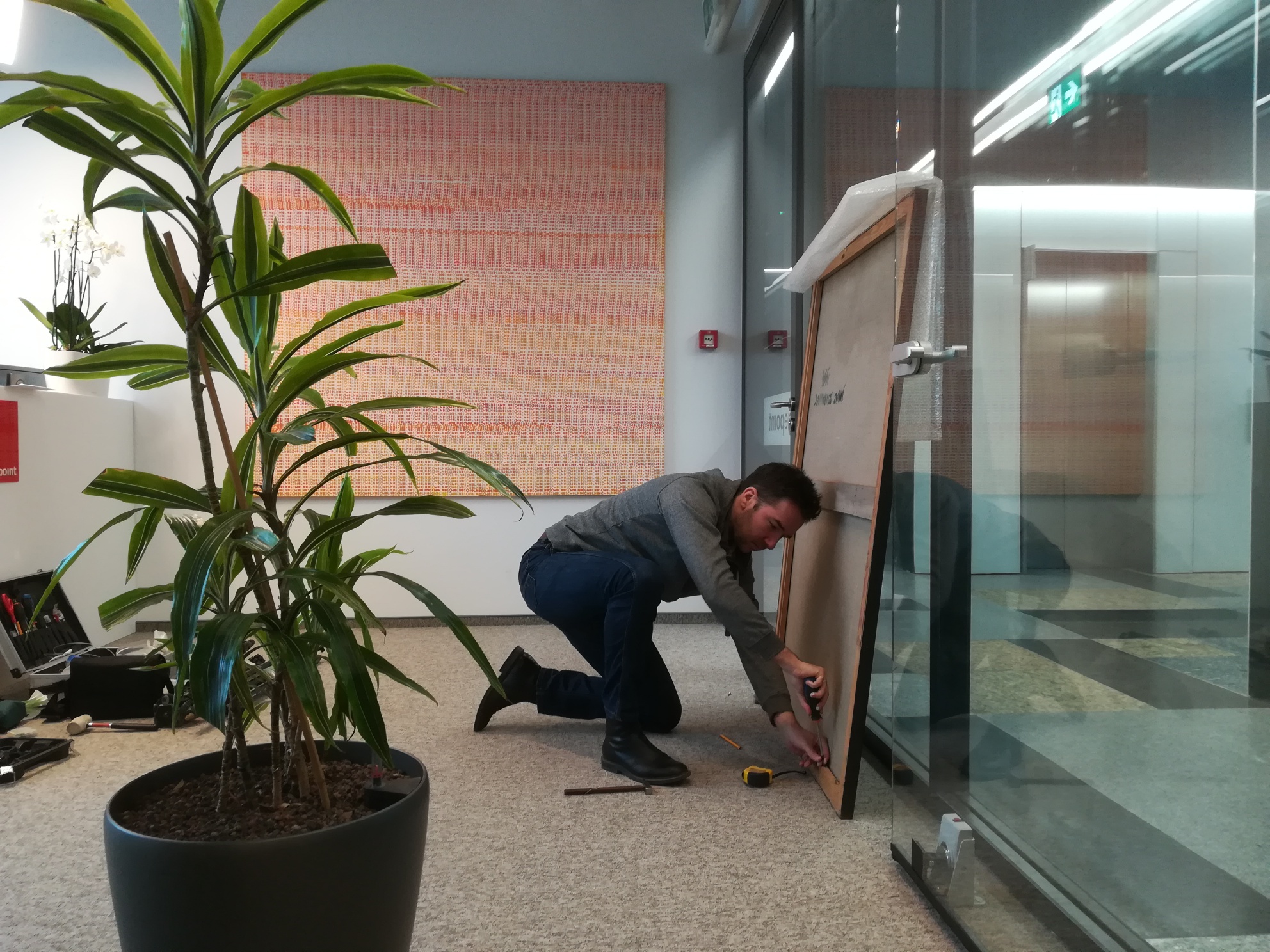 osoba przygotowująca obraz do zawieszenia we wnętrzu biura